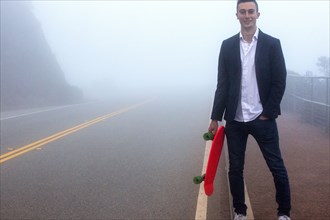 Caucasian man holding small red skateboard in fog