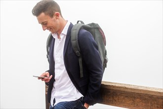 Caucasian man wearing backpack texting on cell phone