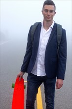 Caucasian man holding small red skateboard in fog