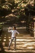 Woman drinking water on sunny forest path