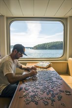 Caucasian man assembling jigsaw puzzle in boat near window