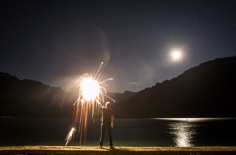 Caucasian man holding sparkler on waterfront at night