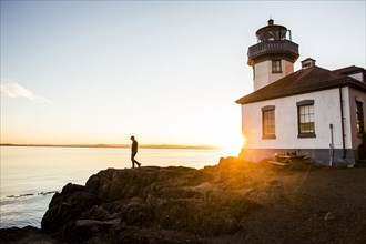 Silhouette of Caucasian man walking on rocks near lighthouse