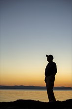 Silhouette of Caucasian man near water at sunset