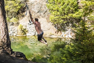 Caucasian man swinging on rope over water
