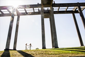 Caucasian brides holding hands walking under concrete structure