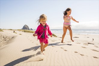 Caucasian sisters running on beach