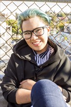 Smiling androgynous Asian woman leaning on chain-link fence