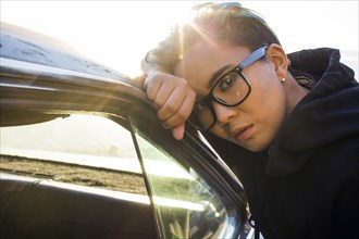 Portrait of serious androgynous Asian woman leaning on car