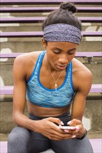 Black woman sitting on bleachers texting on cell phone