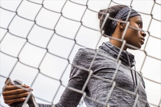 Black woman stretching leg behind chain-link fence