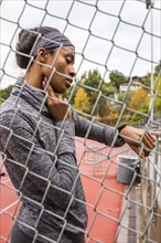 Black woman behind chain-link fence checking pulse