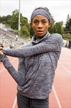 Serious Black athlete stretching arms on track