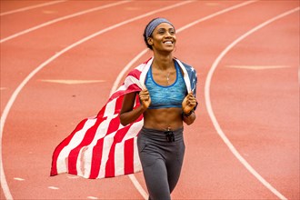 Smiling Black athlete holding American flag on track