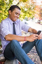 Smiling Mixed Race man sitting on curb texting on cell phone