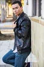 Serious Mixed Race man leaning on wall wearing leather jacket