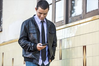 Mixed Race man wearing leather jacket texting on cell phone