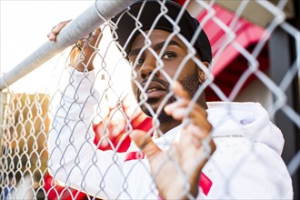 Curious Black man leaning on chain-link fence