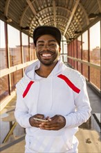 Smiling Black man holding cell phone on footbridge