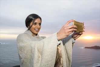 Indian woman posing for cell phone selfie near ocean