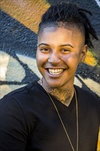 Portrait of androgynous Mixed Race woman smiling near graffiti wall
