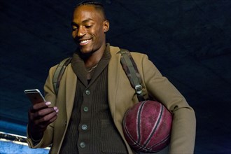 Black man holding basketball texting on cell phone
