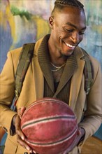 Laughing Black man wearing backpack holding basketball