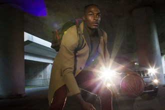 Headlights shining on Black man wearing backpack playing basketball