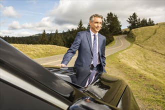 Smiling Caucasian businessman leaning on car