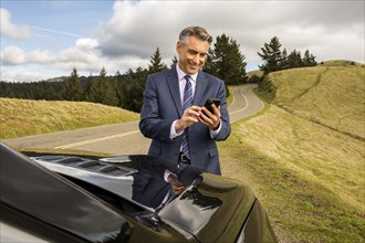 Smiling Caucasian businessman near car texting on cell phone