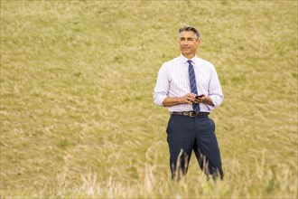 Caucasian businessman standing in grass holding cell phone