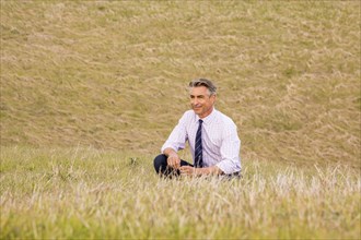 Serious Caucasian businessman crouching in grass