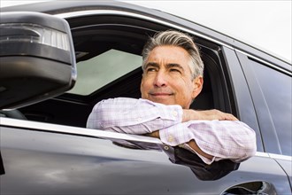 Smiling Caucasian businessman leaning on car window