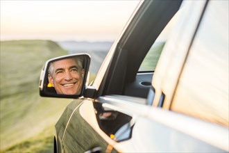 Reflection in mirror of smiling Caucasian man driving car