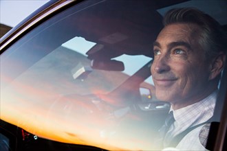 Smiling Caucasian businessman driving car admiring sunset