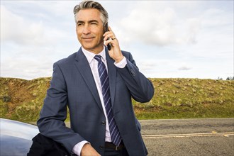 Caucasian businessman leaning on car talking on cell phone