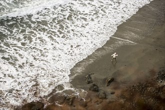 Distant Caucasian woman throwing stone on ocean beach