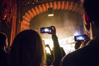 People photographing with cell phones at concert in theater