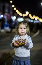 Caucasian girl eating donut outdoors at night