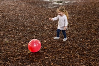 Caucasian girl playing with red ball in autumn