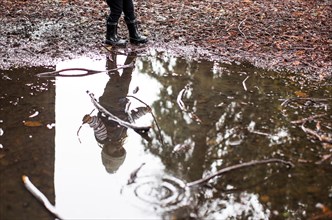 Reflection in puddle of Caucasian girl holding sticks