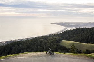 Person with motorcycle at edge of cliff near ocean