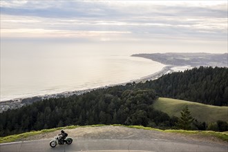 Person riding motorcycle at edge of cliff near ocean