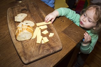 Caucasian girl reaching for cheese near bread on cutting board