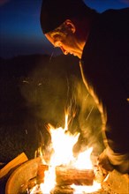 Caucasian man stoking campfire at night