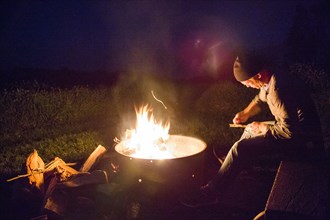 Caucasian man whittling wood near campfire at night