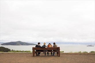 Friends sitting on bench admiring scenic view of ocean