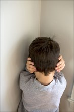Mixed Race boy standing in corner covering ears