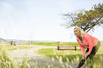 Older Caucasian woman stretching leg in park