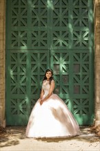 Hispanic girl wearing gown standing near green wall